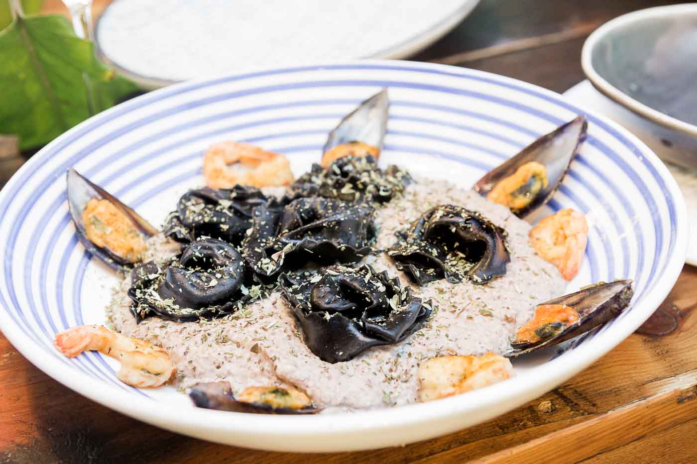 Ravioli negro relleno de salmón con salsa de setas, gambones y mejillón de media concha
